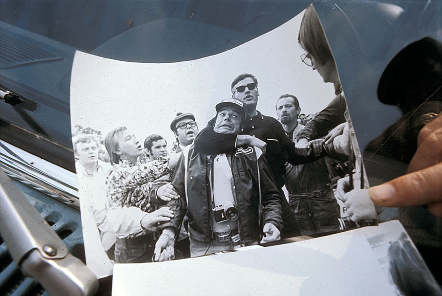 An overeager uninformed security tries to remove Bernard Cahier by headlock from a place where he was allowed to (and insisted to) stay with the helping hands of surrounding spectators