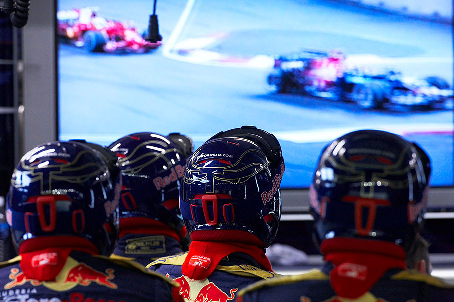 Toro Rosso mechanics watch their car racing on a screen in pits
