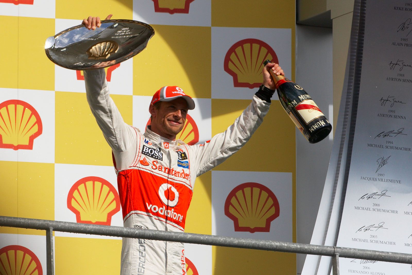 Race winner Jenson Button of McLaren presents his trophy on the podium after the ceremony