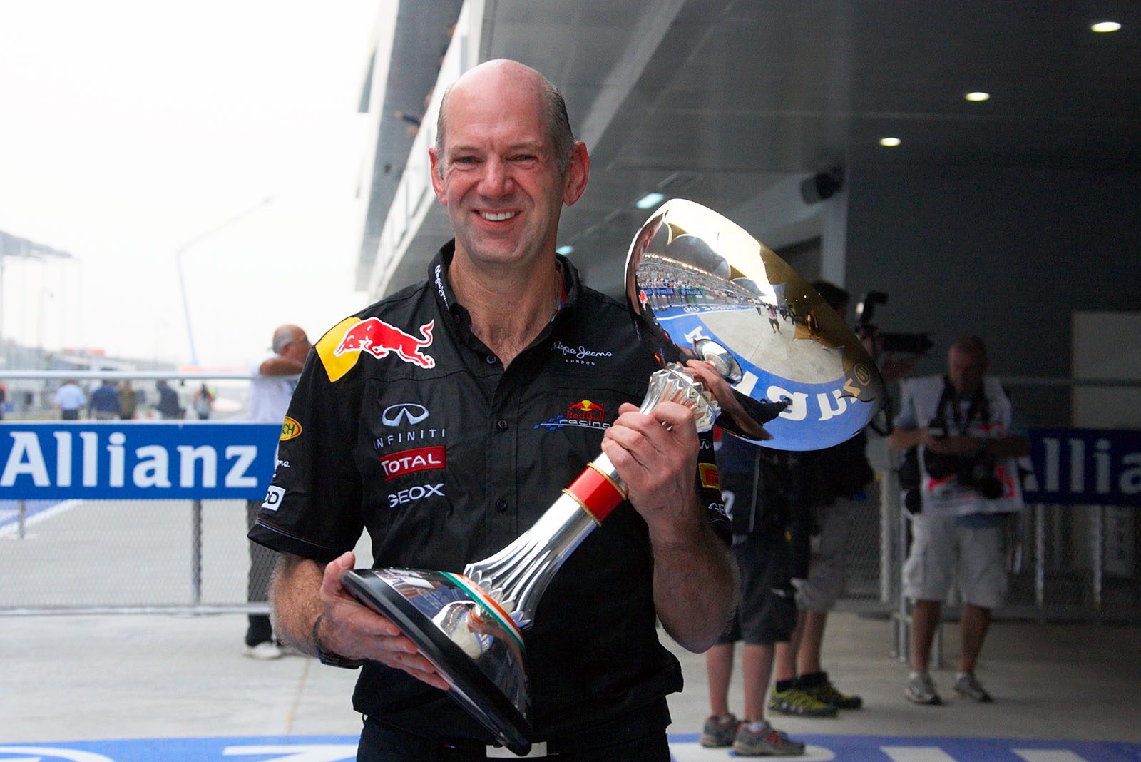 A champagne-soaked Red Bull Racing technical director, Adrian Newey, proudly presents the shiny trophy for the winning constructor after the podium ceremony