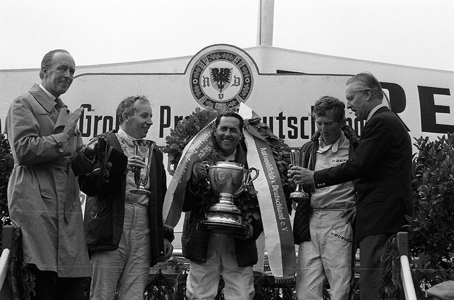 AvD's race director Baron Leo von Diergardt (left hand) claps on the podium for winner Jack Brabham, second placed John Surtees and third placed Jochen Rindt who is given the trophy to by Fuerst von Metternich