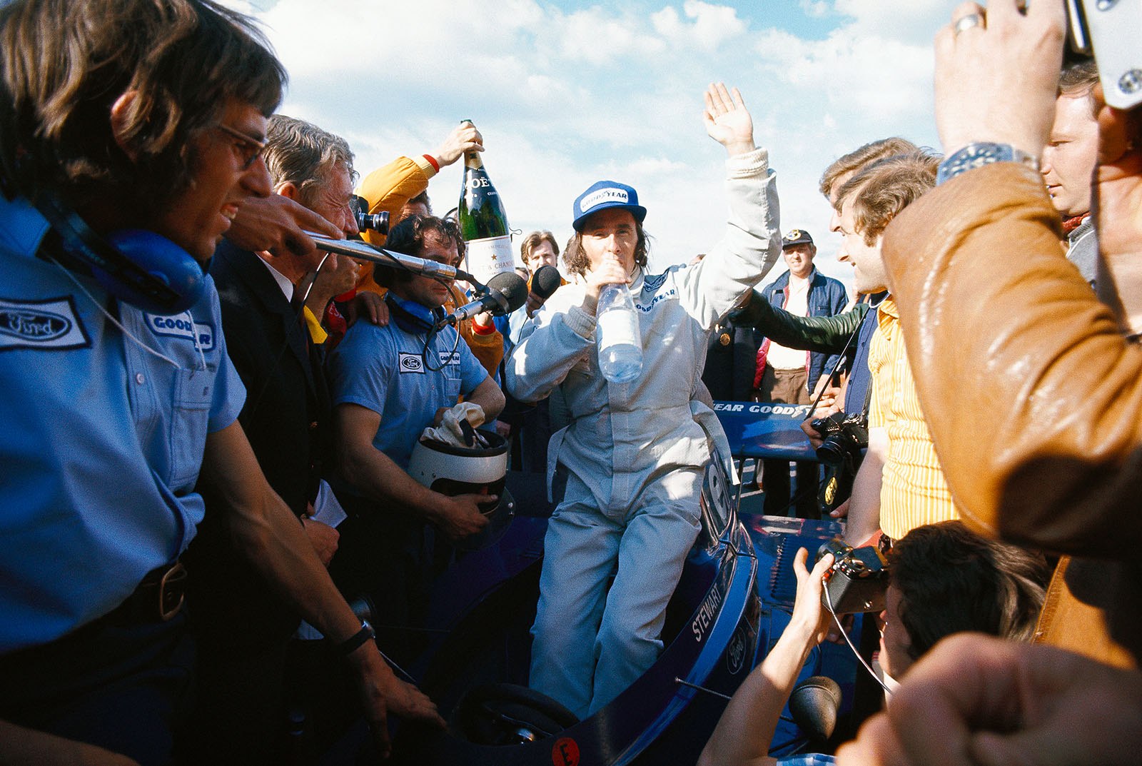 Race winner Jackie Stewart, sitting on the Tyrrell-Cosworth 006, is being warmly welcomed after the race by the cheering media and team members