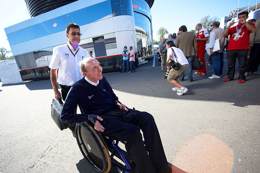 Sir Frank Williams and his physiotherapist arrive in the paddock