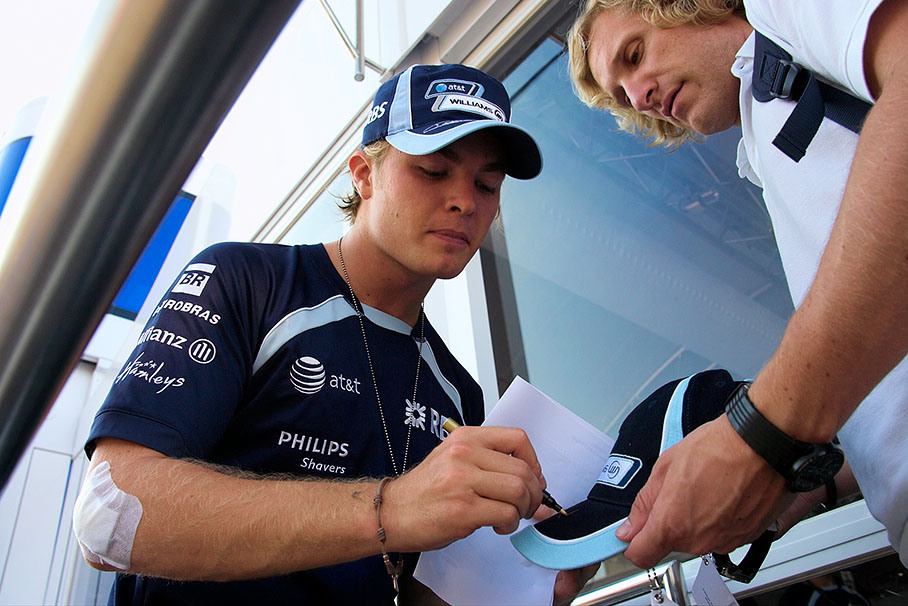 Williams driver Nico Rosberg, also slightly injured, autographs a cap with his physio Oliver Fengler